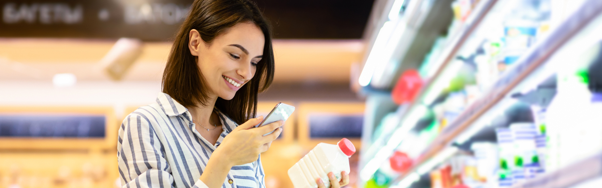 Junge Frau im Supermarkt scannt mit dem Smartphone eine Getränkeflasche im Kühlregal.