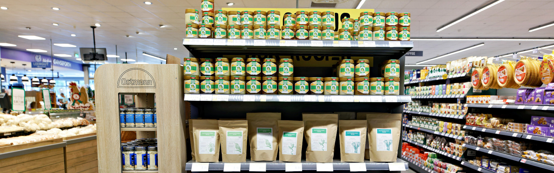 Regal im Combi Markt mit regionalen Produkten: vorne Honiggläser und Kaffeepackungen, daneben ein Ostmann-Gewürzdisplay.