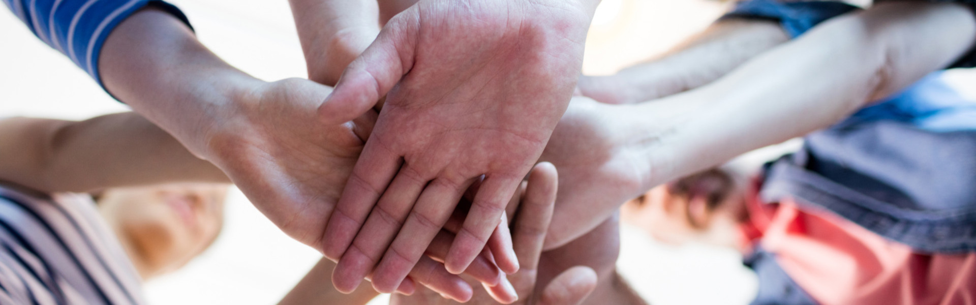 Mehrere Menschen legen ihre Hände übereinander als Symbol für Teamwork und Zusammenhalt.